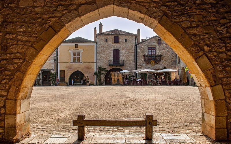 A bastide village square seen through a stone arch