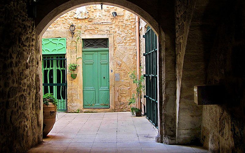 A green door in a sunlit stone courtyard